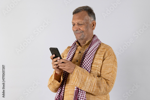 Indian rural old man using mobile at studio background - elder villager using phone - Concept of senior rural people using technology and smartphone