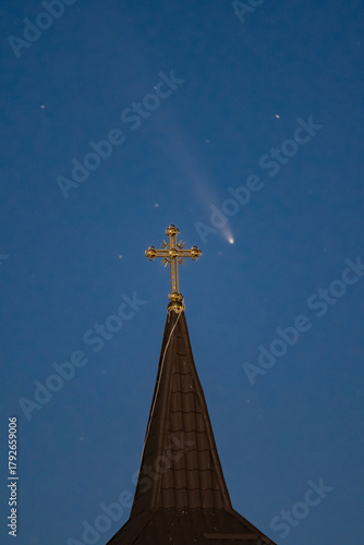 Celestial and Spiritual: Rare Comet ATLAS 2024 Shines Brightly in the Night Sky Behind the Illuminated Cross of an Old Wooden Church, Symbolizing Faith and Science