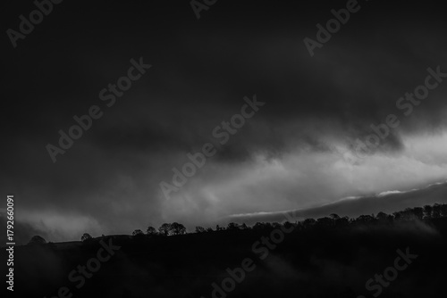 Tableau sur toile Black and white hillside silhouettes under dramatic cloud