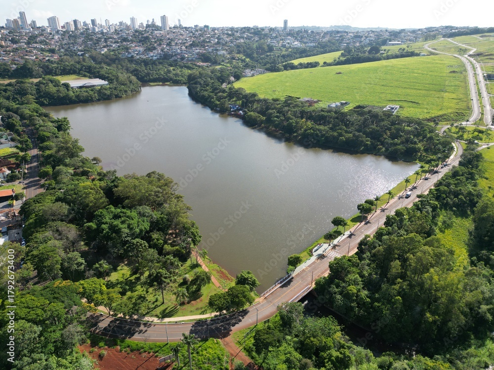Obraz premium Aerial View of a Lake and Urban Area Surrounded by Green Fields and Trees. Concept of urban nature, sustainability, and environmental balance.