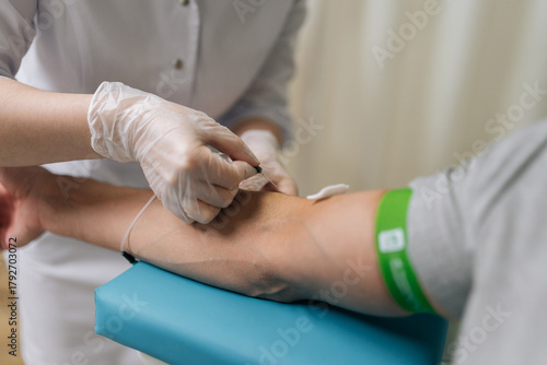 Medical professional in sterile gloves inserts needle into male patient arm vein to collect blood into tube for routine testing, diagnostic laboratory analysis, close-up. Concept of healthy lifestyle