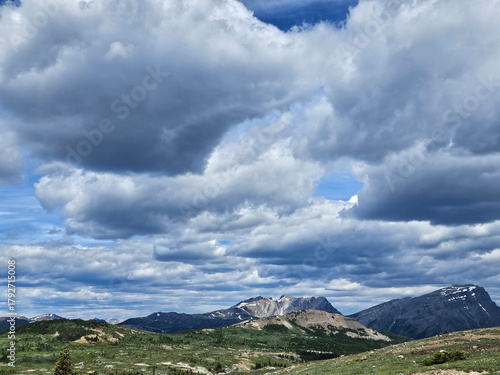 Nature outdoor alpine landscape taken on top of the mountain peak with green grass and a dramatic sky filled with clouds.