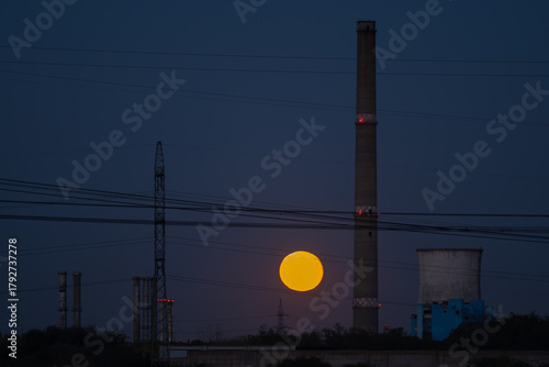 Dramatic Full Moon Rising Between Tall Industrial Chimneys and Cooling Towers at Twilight, Symbolizing Energy, Contrast, and Pollution