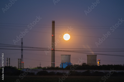 Dramatic Full Moon Rising Between Tall Industrial Chimneys and Cooling Towers at Twilight, Symbolizing Energy, Contrast, and Pollution