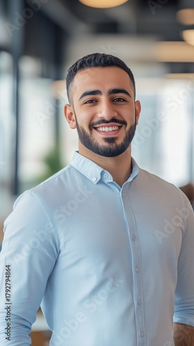 Young Man in Light Blue Shirt Smiling Confidently in a Modern Office Setting ...
