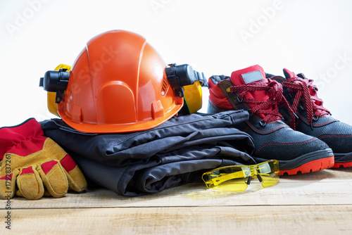 Safety helmet, safety shoes, safety suit, earmuffs, goggles cutresistant gloves on wooden table. Work safety protection equipment.