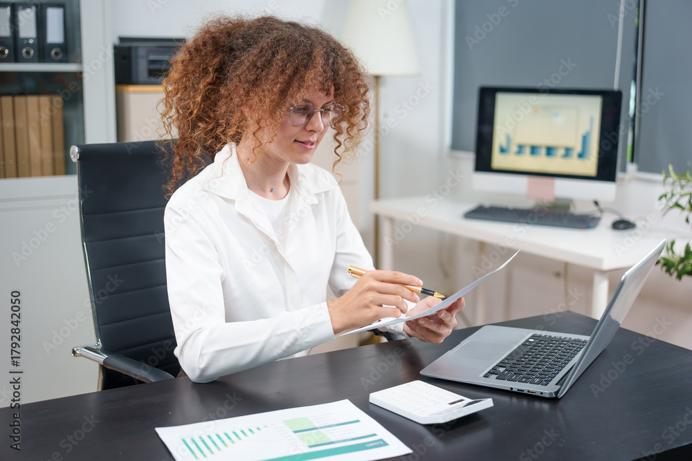 Obraz premium Businesswoman smiling while using laptop and talking on mobile phone at desk in office and at home or coffee shop.