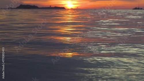 Gentle waves lap the shore at Tanjung Kelayang Beach, Belitung, Indonesia, during a stunning golden sunset. The intricate ripples reflect the warm evening light, creating a peaceful atmosphere