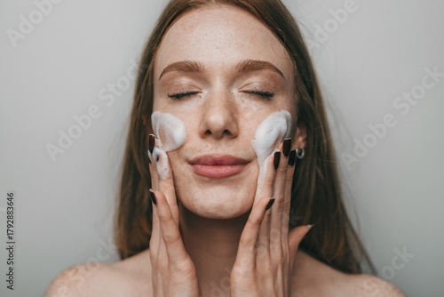caucasian woman using foam cleanser with eyes closed during peaceful morning skincare ritual
