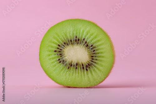 A vibrant green kiwi slice with a white center and numerous small black seeds, displaying its circular pattern. The kiwi's texture contrasts against its fuzzy brown skin on the edges