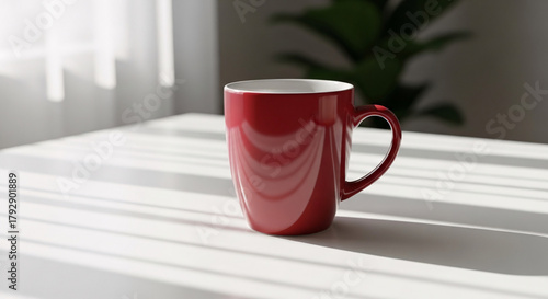 Tall red ceramic mug with handle casting shadows on a white tablecloth