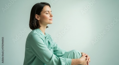 A serene woman sits in a meditative pose, eyes closed, in a softly lit green space, promoting relaxation and mindfulness.
