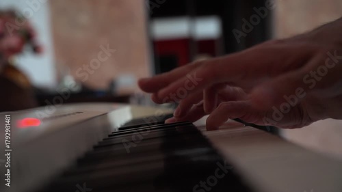 Closeup view of hands playing piano with shallow depth of field, selective focus, and soft bokeh. Side angle of domestic music practice
