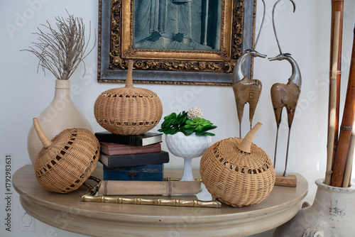 Autumn tabletop vignette with wicker pumpkins, vintage books, and white compote planter, natural light, thanksgiving and fall decor