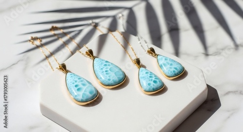 Beautiful larimar gemstone pendants and earrings on a white marble surface with palm leaf shadow  for national larimar day