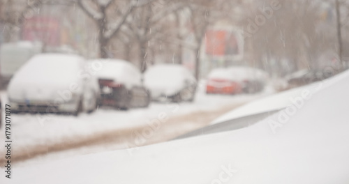 Gentle snow falls over a busy city landscape, blanketing cars and streets in a serene winter scene. The quiet charm of the snow transforms the familiar surroundings.