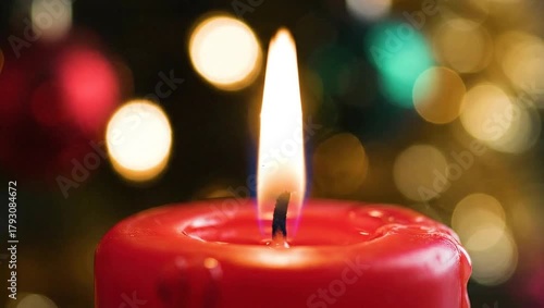 A close-up shot of a red candle burning with a flickering flame, set against a blurred background of colorful Christmas lights.