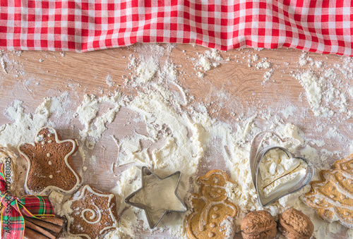 Christmas cookies making: flour, cake pans, nuts, gingembread and checkered napkin on a wooden table; copy space