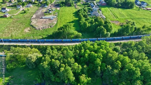 Dynamic aerial 4K footage of railway tracks as a long freight train approaches, carrying cargo wagons through industrial landscape.