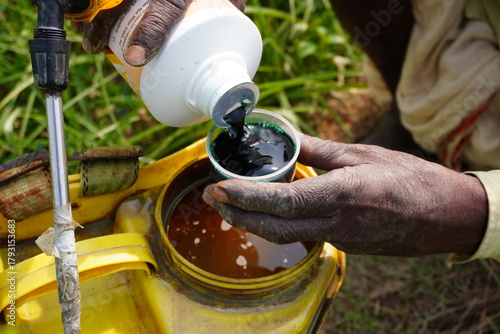 Hand pouring pesticide concentrate into agricultural sprayer tank