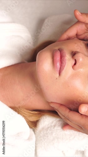 blonde caucasian woman receiving facial massage, esthetician's hands gently contouring chin and jawline on white towel, dewy skin glow, soft lighting, serene spa atmosphere, massage in spa center