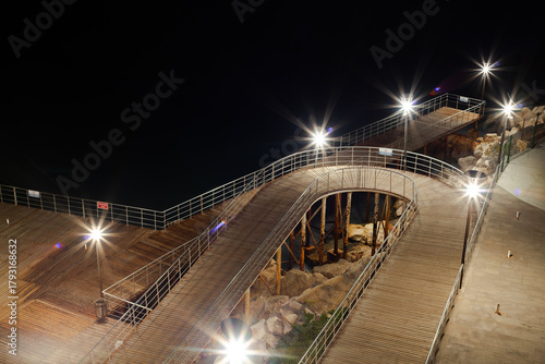 Fototapeta Naklejka Na Ścianę i Meble -  Wooden pier and walkways built on metal poles by the sea. The wooden pier and walkway are illuminated at night.