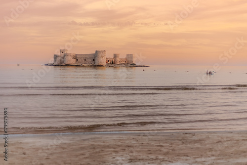 Fototapeta Naklejka Na Ścianę i Meble -  The famous historical Maiden's Castle in Mersin, Turkey. Maiden's Castle in a sunset view. Known as Kız Kalesi in Turkish. Tourists paddle boarding. Erdemli, Mersin, Türkiye - October 23, 2025.