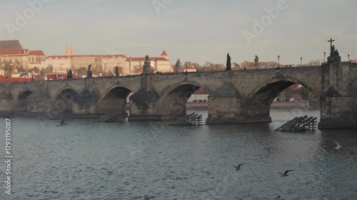 Wide sunrise footage of the historic Charles Bridge crossing the Vltava River, with a clear view of Prague Castle and St. Vitus Cathedral illuminated in the background. Shot in Prague, Czech Republic.