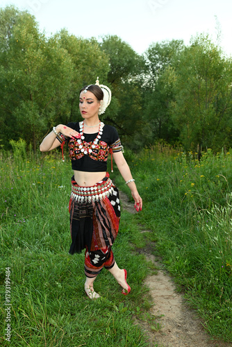Indian female dancer in a beautiful costume on a green nature background in a park
