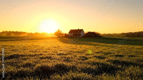 Golden sunrise over a field of grass, illuminating a house in the distance