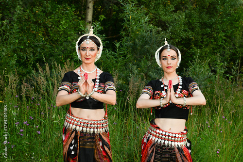 Indian female dancers in beautiful costumes on a green background of nature in a park in dance poses