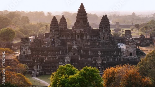 Iconic angkor wat temple standing amidst the lush jungle during a hazy, golden sunset. Aerial view of the ancient khmer architecture. UNESCO World Heritage Site