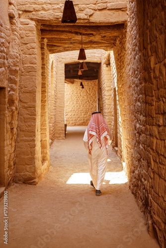 Saudi Arabia. Man dressed with typical Saudi clothes walks thru small street in Old Town Al Ula. 