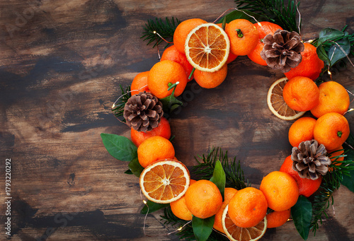 Wreath of fresh ripe tangerines with leaves and cones, on wooden background, top view