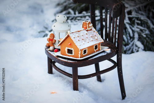 Gingerbread house and holiday decoration on chair in snow winter outdoor background