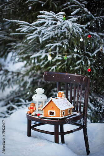 Gingerbread house and holiday decoration on chair in snow winter outdoor background