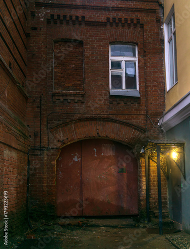 Old red brick wall with iron door and white window in the alley