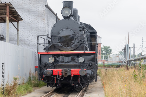 A steam locomotive on a siding next to a grey fence