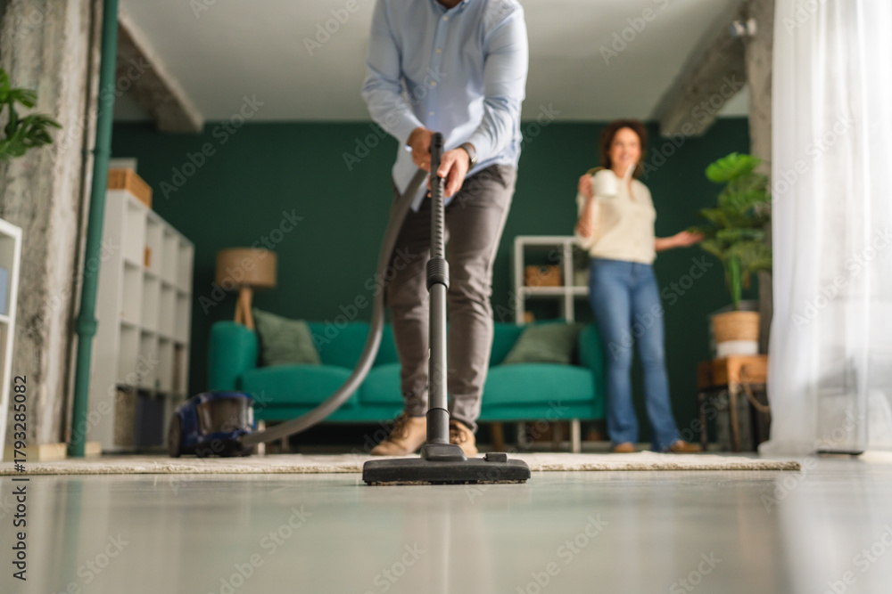 Fototapeta premium Man vacuuming living room floor while woman watches