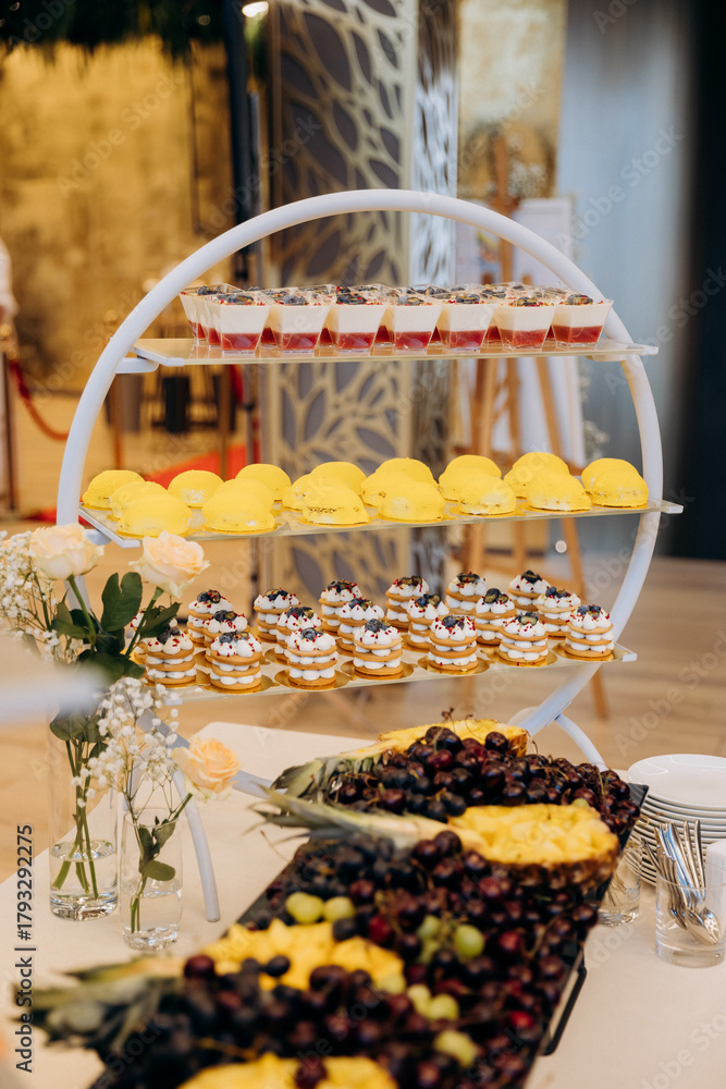 Naklejka premium Tiered dessert stand with panna cotta mousse domes and mini cakes at elegant reception