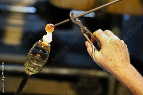 A glass crafter is burning and blowing an art piece.