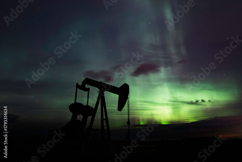 Oil pump jack silhouette against Aurora Borealis background.

