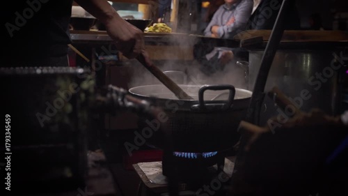 Slow motion showing an illuminated row of yatai food stalls with diners eating under warm lights at night in Fukuoka, Japan, creating a cozy street food atmosphere
