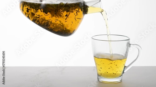 Pouring herbal tea into transparent cup from teapot