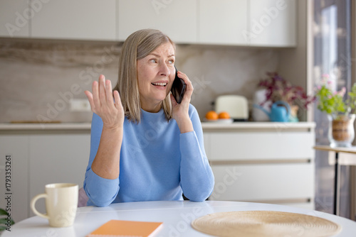 Quadro em tela Senior woman in modern kitchen looks upset and gestures while on a frustrating p