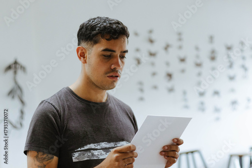 Young male art student reading document in classroom, concentrating on college assignment or creative project