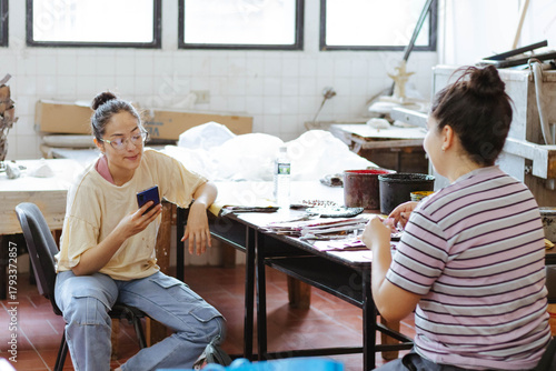 Art students using phone and chatting in studio, learning creative skills, collaborating on project, preparing artwork