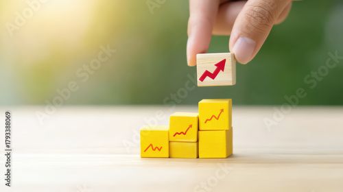 Hand placing wooden block with red upward arrow on top of yellow blocks with similar arrows, symbolizing growth and progress in business or finance