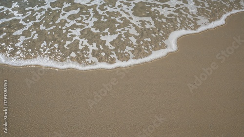 Fototapeta Naklejka Na Ścianę i Meble -  Close-up of gentle wave wash on sandy beach with foam patterns. Nature and sea, concept. Ocean and shoreline. The themes of tranquility and coastal environment.