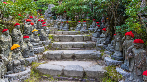 Quadro su tela Buddha with red and yellow caps along a path in garden of Buddha temple Takifudo